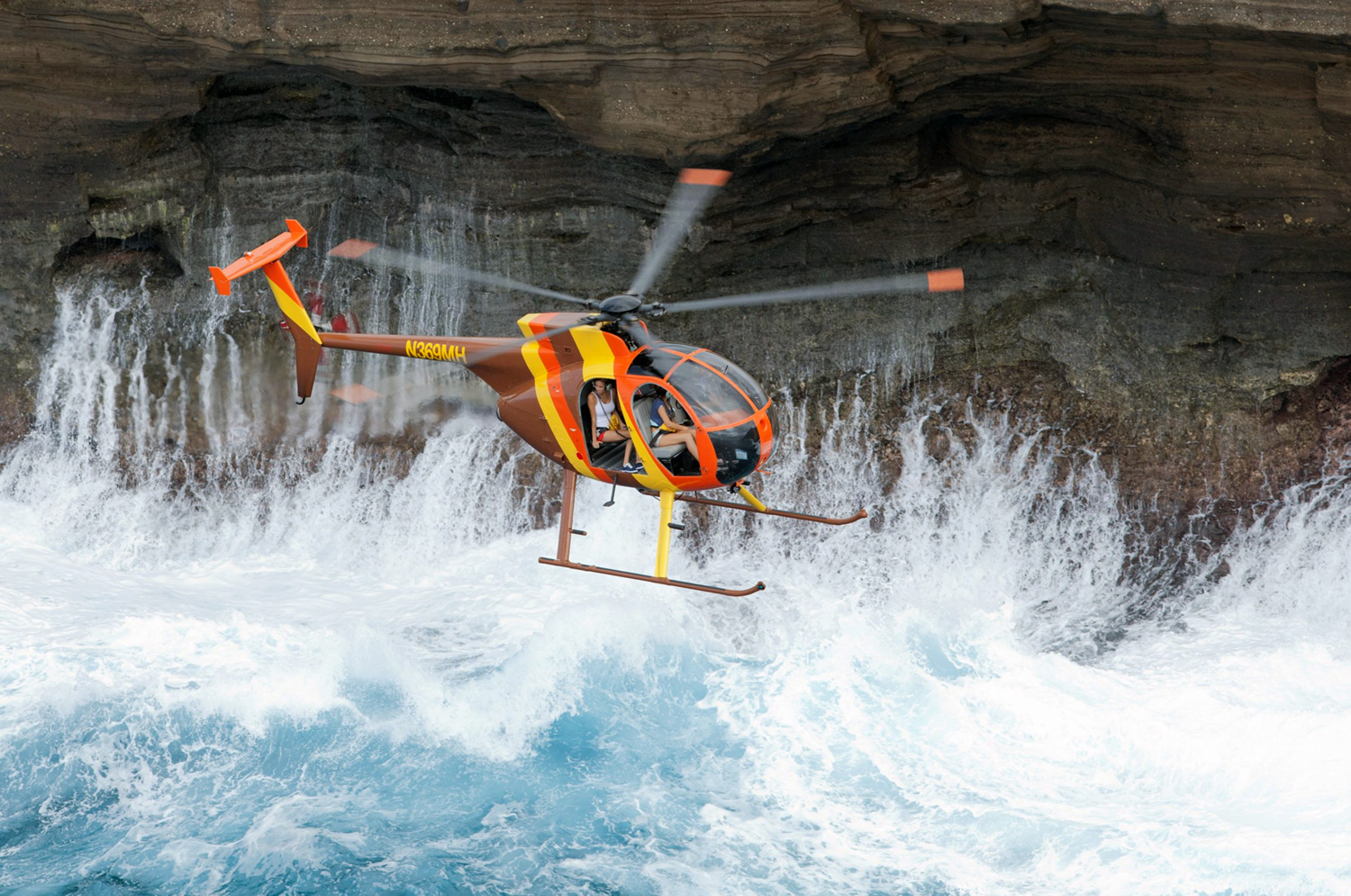 Shot from above, this Hughes 500 is dressed to the 9s in the famous Magnum P.I. color scheme as it’s photographed against seaside cliff as the faces of tourists peer at the cameraship lens