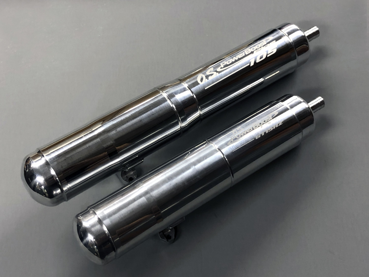 Close up photo of both the OS MAX PowerBoost Pipe 105 versus PowerBoost Pipe GT15HZ exhaust systems showing the former is a lot larger.